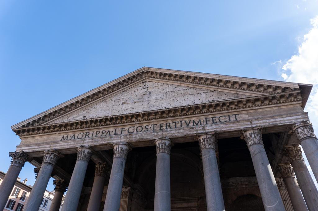 The front facade of the Pantheon in Rome, showing its classical portico with granite columns and the Latin inscription M·AGRIPPA·L·F·COS·TERTIVM·FECIT against a blue sky.
