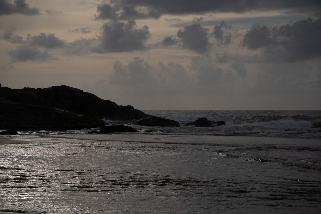 Rocky coastal headland silhouetted against sparkling ocean water under dramatic cloudy sky